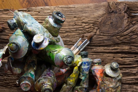 Vintage stylized photo of oil multicolor paint tubes closeup and artist paintbrushes on wooden desk. Top view.の写真素材