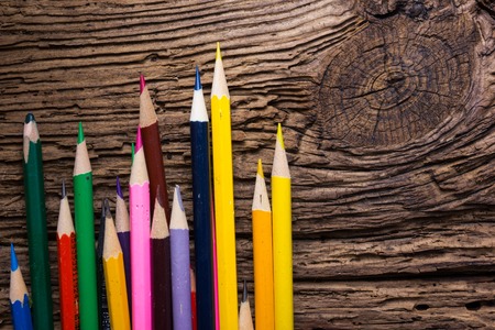 Row of colored drawing pencils closeup on old grunge natural wooden shabby desk background. Vintage...
