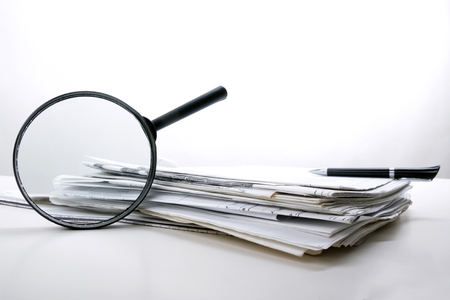Search with magnifying glass in books, blueprints, magazines looking for information. Audit inspection. Copy space for text. Isolated on white backgroundの写真素材