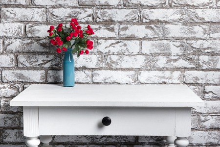 Red flowers in vase on the table on black and white brick wall background.