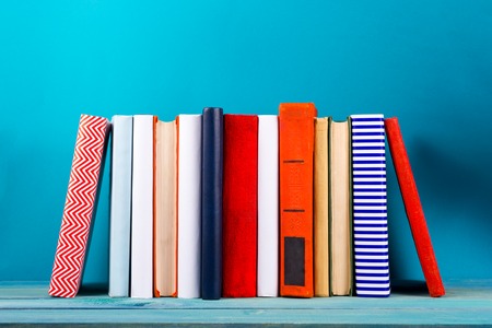 Stack of colorful books, grungy blue background, free copy space Vintage old hardback books on wooden shelf on the deck table, no labels, blank spine. Back to school. Education backgroundの写真素材