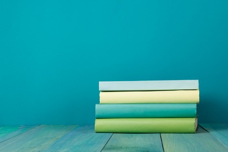 Stack of colorful books, grungy blue background, free copy space Vintage old hardback books on wooden shelf on the deck table, no labels, blank spine. Back to school. Education backgroundの写真素材