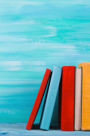 Stack of colorful books, grungy blue background, free copy space Vintage old hardback books on wooden shelf on the deck table, no labels, blank spine. Back to school. Education backgroundの写真素材