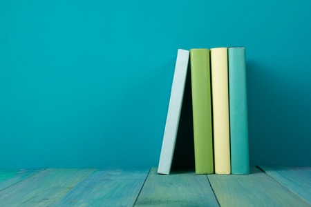 Row of books, grungy blue background, free copy space Vintage old hardback books on wooden shelf on the deck table, no labels, blank spine. Back to school. Education background