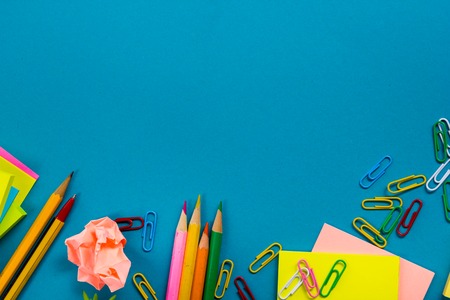 Office table desk with set of colorful supplies, white blank note pad, cup, pen, pc, crumpled paper, flower on blue background. Top view and copy space for text.の写真素材