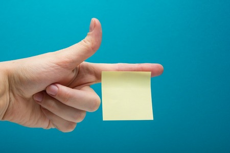 Hand holding yellow note reminder on finger with copy space for ad on blue background