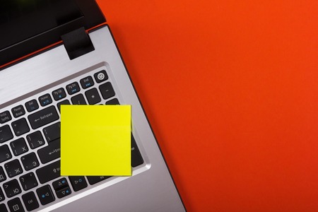 Office table desk with set of colorful supplies, laptop and reminder sticky note on red background....