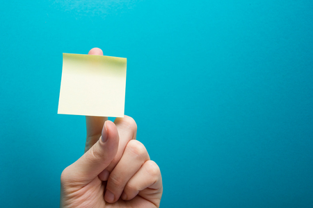 Hand holding yellow note reminder on finger with copy space for ad on blue backgroundの写真素材