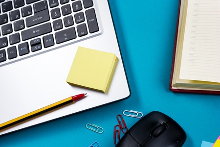 Office table desk with set of colorful supplies, white blank note pad, cup, pen, pc, crumpled paper,...