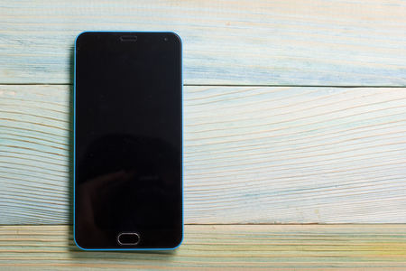 Smartphone with blank area on touch screen rustic wood blue table at outdoor in morning time, high contrast natural lighting.の写真素材