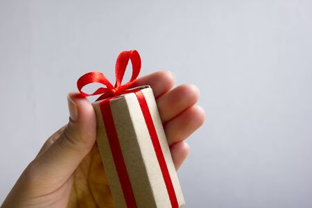 Female hand holding present gift box against grey background. Happy family celebrating concept for Valentine Birthday Christmas or New Years dayの写真素材