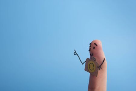 Funny finger tourist holding a camera and smiling against blue background with copy space for ad textの写真素材