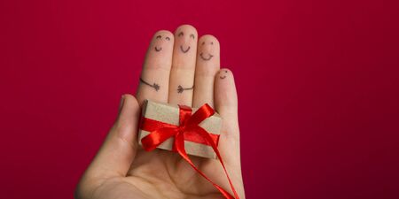 Funny fingers faces present gift box against red background with copy space for text. Happy family...