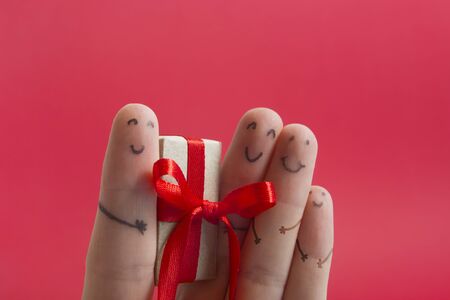 Funny fingers faces present gift box against red background with copy space for text. Happy family celebrating concept for Christmas or New Years dayの写真素材