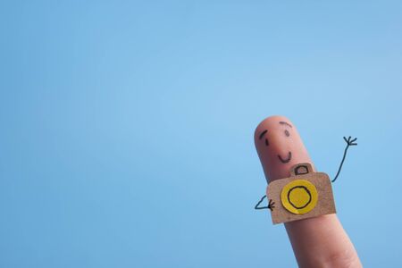 Funny finger tourist holding a camera and smiling against blue background with copy space for ad textの写真素材