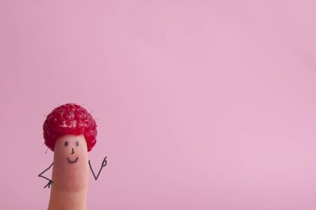 Funny fingers faces in hat raspberries berry against pink background. Happy family couple healthy eating concept.の写真素材