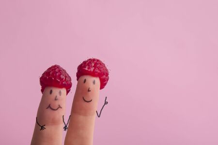 Funny fingers faces in hat raspberries berry against pink background. Happy family couple healthy eating concept.の写真素材