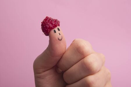Funny fingers faces in hat raspberries berry against pink background. Happy family couple healthy eating conceptの写真素材
