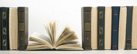 Composition with vintage old hardback books, diary, fanned pages on wooden deck table and red background. Books stacking. Back to school. Copy Space. Education backgroundの写真素材
