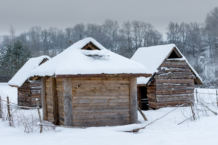 Historical peasant huts snowy winter forest in the meadow in winterの写真素材