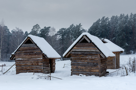 Historical peasant huts snowy winter forest in the meadow in winterの写真素材