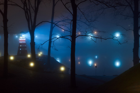 The light from the shore lights reflected in the water. Coast of light reflections in the water mist. In late autumn foggy night shore light reflected in the water.の写真素材