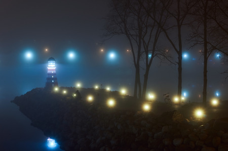 The light from the shore lights reflected in the water. Coast of light reflections in the water mist. In late autumn foggy night shore light reflected in the water.の写真素材