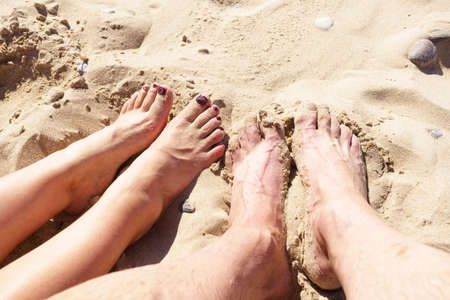 Women and man's legs in the sea sand, photographed nearby, from above, varnished toenails, sandy beach, recreation by the seaの写真素材