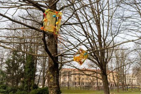 A deciduous tree with yellow flowers, adorned with Easter eggs hanging from its branches, creating a...
