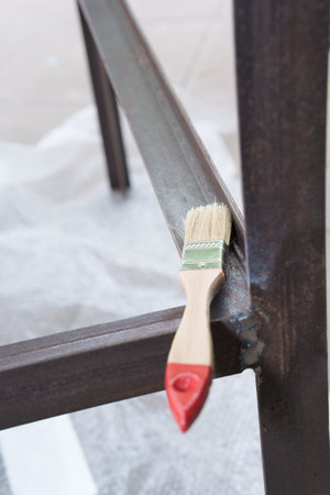 In a canopy in the yard, the owner paints a metal structure black with a brush on a concrete base, gloves on his hands on a sunny and summer day, home renovation with his own handsの写真素材