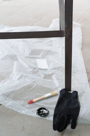 In the yard, a person paints a metal structure black with a brush on a concrete base, wearing gloves on his hands on a sunny and summer day, home renovation with his own handsの写真素材