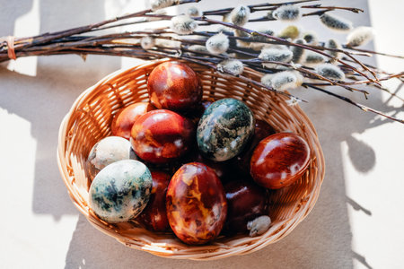 Top view of traditional colored Easter eggs in a wicker basket with pussy willows. Sunny spring composition with hard shadows.の写真素材