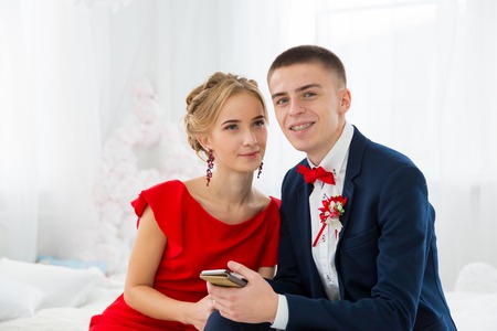 A girl in a red dress with a guy holding a mobile phone.の写真素材
