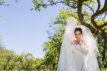 A fantastic bride in the park sits on the swing and looks at the wedding dressの写真素材