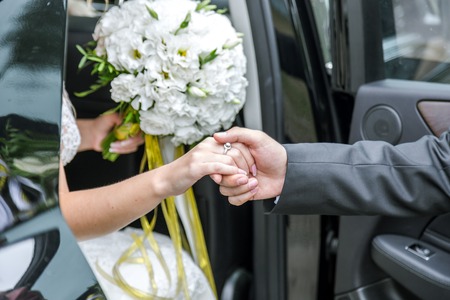 Groom holds the brides hand out of the car