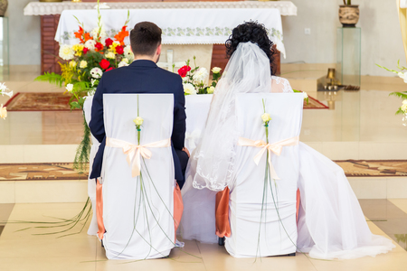 Wedding ceremony. Bride and groom during the wedding sit in the church on the chairsの写真素材