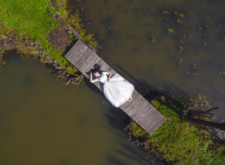 The bride is lying on a wooden bridge, barefoot. Top viewの写真素材