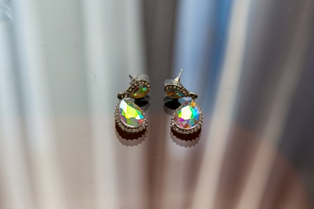Earrings with diamonds macros are lying on the glass and shine in the sun in different colors.