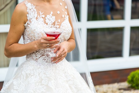 Beautiful young bride with martini glass. The brides hand and a glass of red beverageの写真素材