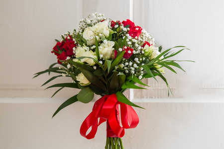 Wedding bouquet of red and white roses, tied with a red ribbon, on the background of white doorsの写真素材