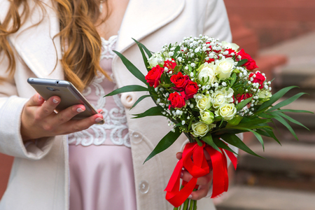The girl holds a phone in her hand, a bouquet in her other handの写真素材