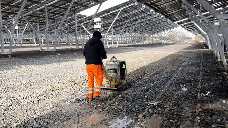 An employee using a vibrating machine compresses the rubble on the future Parking lot under the...