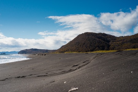 Halaktyr beach. Kamchatka. Russian federation. October of 2017. Dark almost black color sand beach of Pacific ocean. Stone mountains and yellow grass are on a background. Light blue sky.の写真素材
