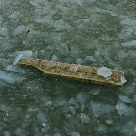Old timber desk is clutched between ice. Picture is in dark depressive colors. Water is frozen around a wood board. Weather is cold winter.の写真素材