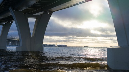 Close up picture of beach's surface. Ice is melted. Some concrete constructions are on a background. Sky is covered by clouds. Some sun lights reflects on melted surface of ice cover. Waves comes.の写真素材