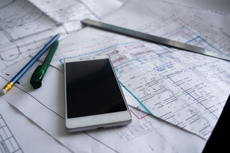 Green pen, blue pencil, white cellphone, metal ruler, notepad and some paper draws of a house (home) are laying down on white table. All staff is for a architecture negotiation.の写真素材
