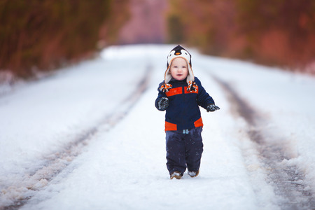 A young boy wearing a winter coat and had smiles as he walks down a snow covered road.の写真素材