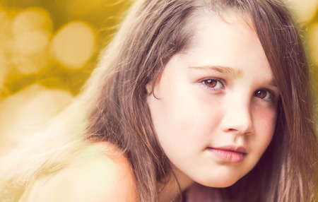 Confident young girl looking at camera smiling on a sunny day with beautiful bokeh backgroundの写真素材