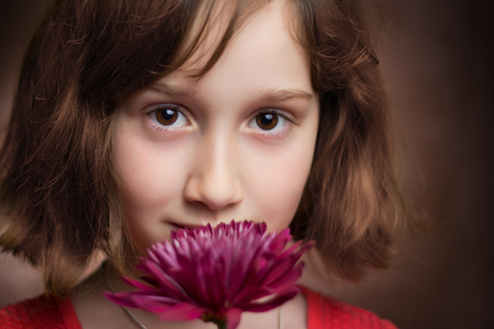 A beautiful young girl holding a pink flower and looking at the camera.の写真素材
