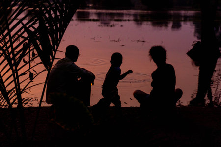 Silhouette of family sitting on the river bank at sunset.の写真素材